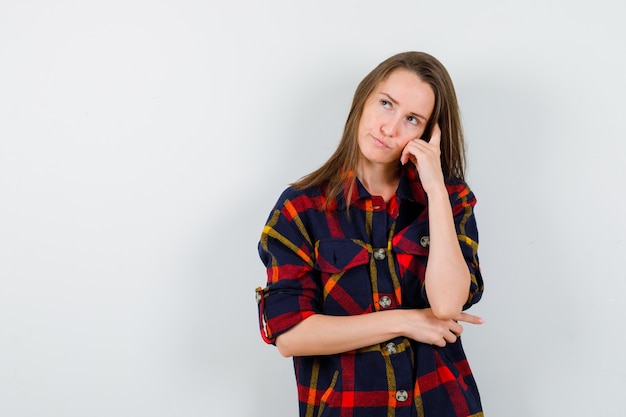 Jonge dame leunend hoofd op hand in casual shirt en op zoek doordachte, vooraanzicht.