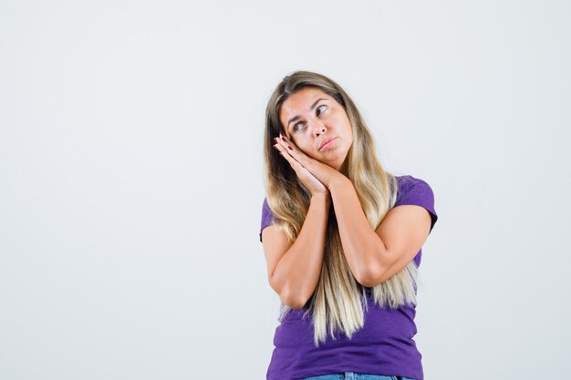 Jonge dame leunend op handpalmen als kussen in violet t-shirt en ziet er schattig uit. vooraanzicht.