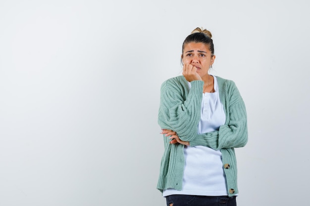 Jonge dame leunt met kin aan de hand in t-shirt, jas en kijkt peinzend