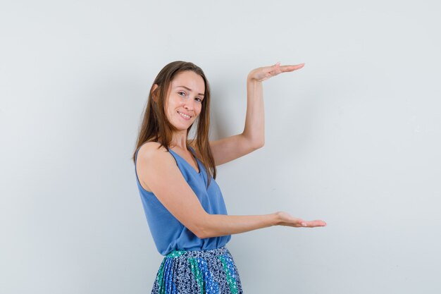 Jonge dame met groot formaat bord in blauwe blouse, rok en op zoek blij, vooraanzicht.