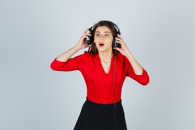 Jonge dame met koptelefoon wegkijken in rode blouse, rok en verbaasd kijken