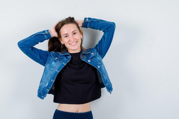 Jonge dame omklemd het hoofd met handen in blouse, jas en ziet er zelfverzekerd uit. vooraanzicht.