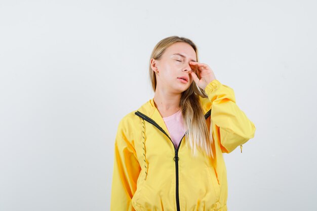 Jonge dame oog wrijven in t-shirt, jasje en slaperig op zoek