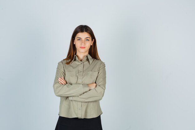 Jonge dame permanent met gekruiste armen in shirt, rok en op zoek zelfverzekerd