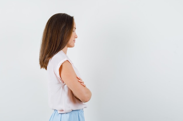 Jonge dame permanent met gekruiste armen in t-shirt, rok en peinzend op zoek. .