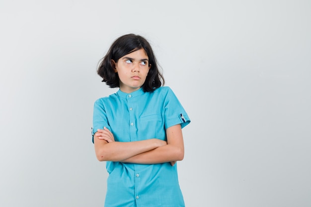 Jonge dame permanent met gekruiste armen terwijl opzoeken in blauw shirt en beledigd kijken.