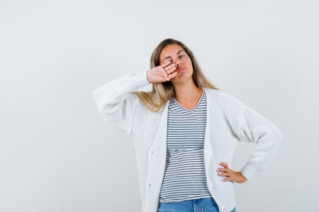 Jonge dame poseren met hand op gezicht in t-shirt, jasje en op zoek naar zelfverzekerd, vooraanzicht.