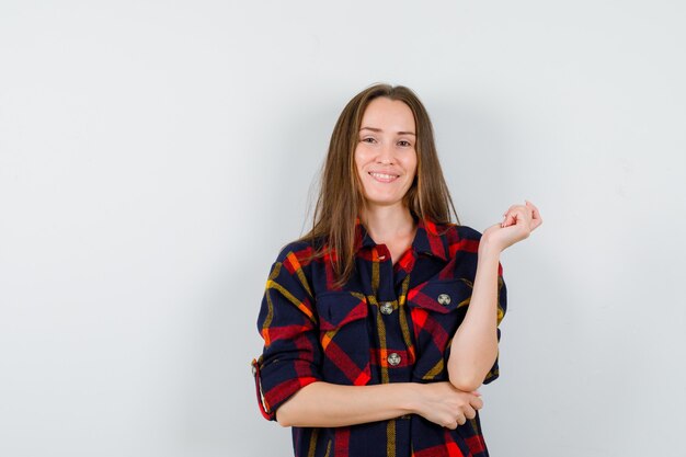 Jonge dame poseren met opgeheven hand in casual shirt en op zoek gelukkig, vooraanzicht.