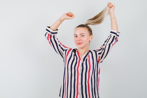 Jonge dame poseren met vliegend haar in een gestreept overhemd en ziet er charmant uit