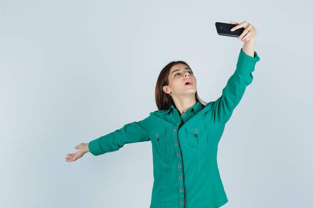 Jonge dame poseren terwijl het nemen van selfie op mobiele telefoon in groen shirt en op zoek gelukkig, vooraanzicht.