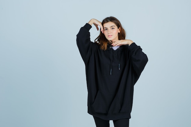 Jonge dame poseren terwijl ze in een oversized hoodie, broek staat en er zelfverzekerd uitziet. vooraanzicht.