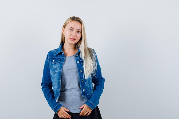 Jonge dame poseren terwijl ze in t-shirt, spijkerjasje, rok staat en er aantrekkelijk uitziet.