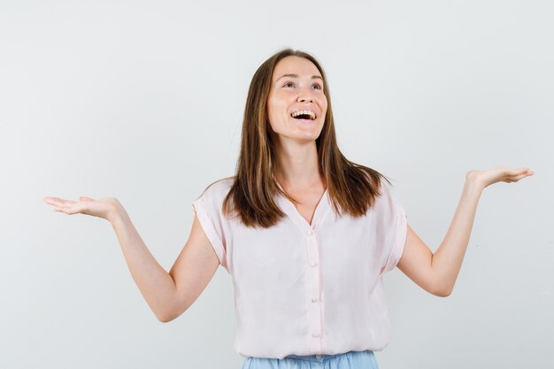 Jonge dame schalen gebaar maken in t-shirt, rok en op zoek gelukkig, vooraanzicht.