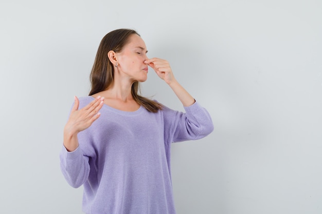 Jonge dame snijdt neus als gevolg van slechte geur in casual shirt en walgt op zoek. vooraanzicht.