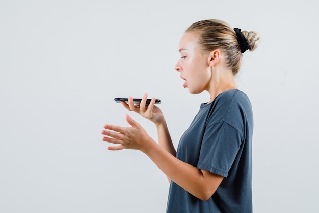 Jonge dame spraakbericht opnemen op mobiele telefoon in grijs t-shirt.