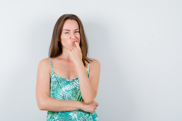 Jonge dame staat in denkende pose in blouse en kijkt besluiteloos. vooraanzicht.