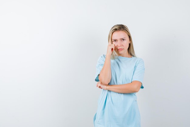 Jonge dame staat in denkende pose in t-shirt en kijkt peinzend geïsoleerd