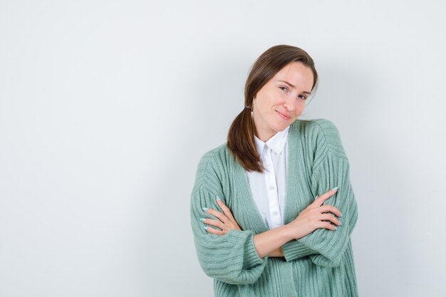 Jonge dame staat met gekruiste armen in blouse, vest en schaamt zich. vooraanzicht.