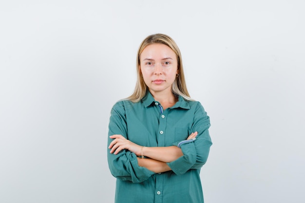 Gratis foto jonge dame staat met gekruiste armen in groen shirt en ziet er zelfverzekerd uit.