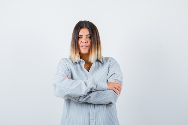 Jonge dame staat met gekruiste armen in oversized shirt en ziet er zelfverzekerd uit, vooraanzicht.