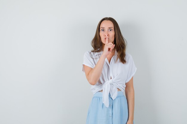 Jonge dame stilte gebaar in witte blouse, blauwe rok tonen en gericht kijken