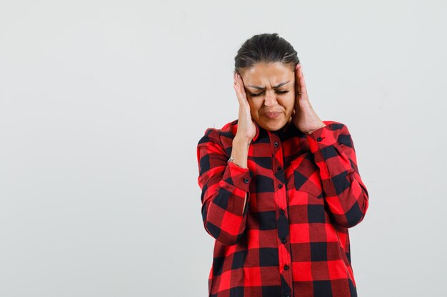 Jonge dame tempels wrijven en hoofdpijn hebben in geruit overhemd