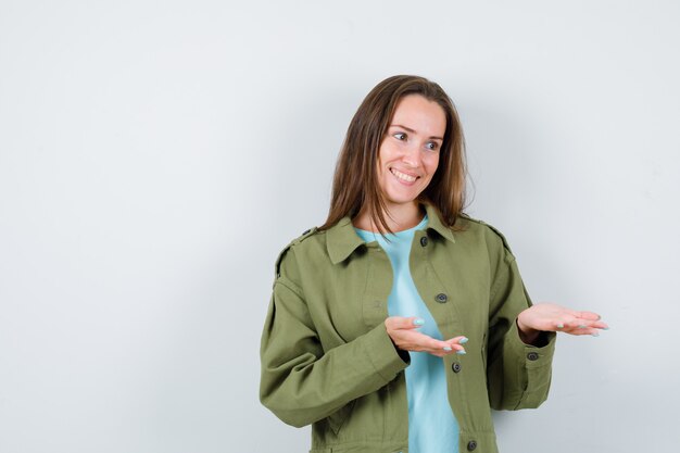 Jonge dame verwelkomt iets in t-shirt, jas en ziet er gelukkig uit. vooraanzicht.