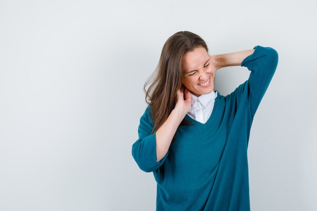 Jonge dame voelt nekpijn in wit overhemd, trui en ziet er ongemakkelijk uit. vooraanzicht.