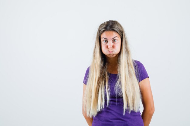 Jonge dame waait wangen in violet t-shirt en kijkt nerveus, vooraanzicht.