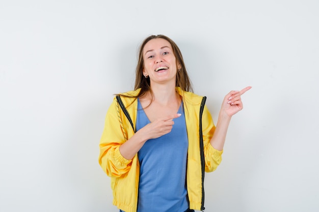 Jonge dame wijst naar de rechterbovenhoek in t-shirt, jas en ziet er zelfverzekerd uit. vooraanzicht.