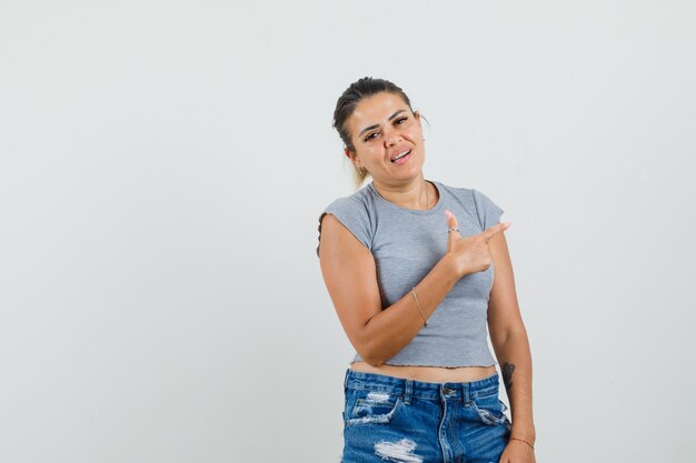 Jonge dame wijst naar de zijkant in t-shirt, korte broek en kijkt zelfverzekerd.