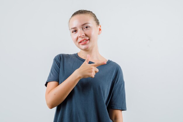 Jonge dame wijst naar kant met pistoolgebaar in grijs t-shirt en kijkt vrolijk