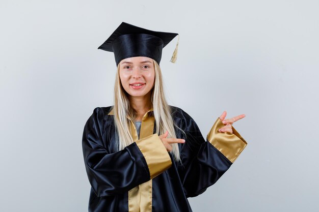 Jonge dame wijst opzij in academische jurk en ziet er aantrekkelijk uit