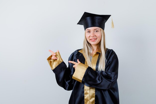 Jonge dame wijst opzij in academische jurk en ziet er gelukzalig uit