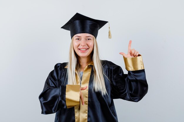 Jonge dame wijst opzij in academische kleding en ziet er zelfverzekerd uit.