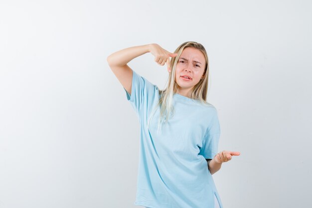 Jonge dame wijst opzij in t-shirt en kijkt aarzelend, vooraanzicht.