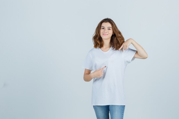 Jonge dame wijst opzij in t-shirt, spijkerbroek en kijkt vrolijk. vooraanzicht.