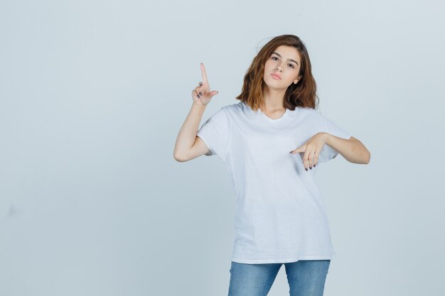 Jonge dame wijst opzij in t-shirt, spijkerbroek en kijkt zelfverzekerd, vooraanzicht.