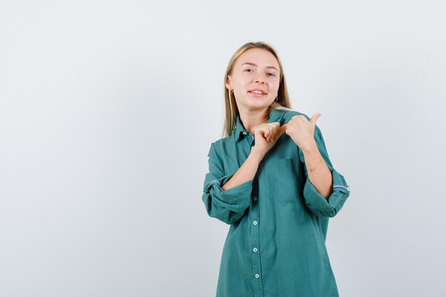 Jonge dame wijst opzij met duimen in groen shirt en ziet er vrolijk uit