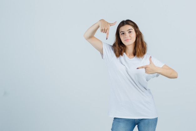 Jonge dame wijst weg in t-shirt, spijkerbroek en kijkt zelfverzekerd. vooraanzicht.