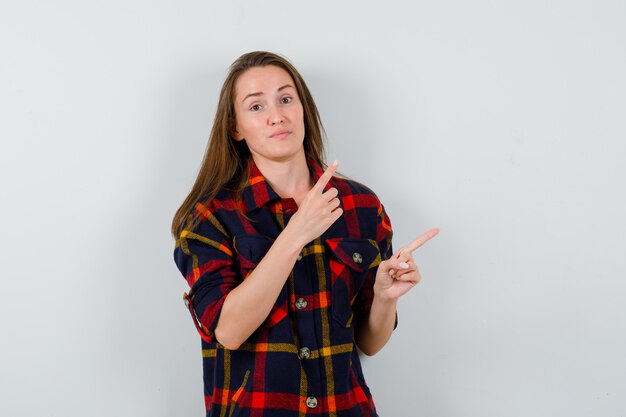 Jonge dame wijzend op de rechterbovenhoek in casual shirt en aarzelend op zoek. vooraanzicht.