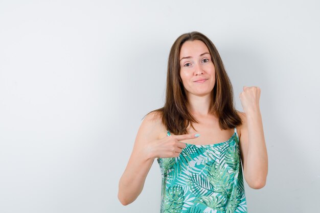 Jonge dame wijzend op opgeheven vuist in blouse en zelfverzekerd, vooraanzicht.