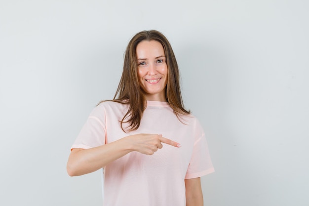 Jonge dame wijzende vinger naar beneden in roze t-shirt en kijkt vrolijk