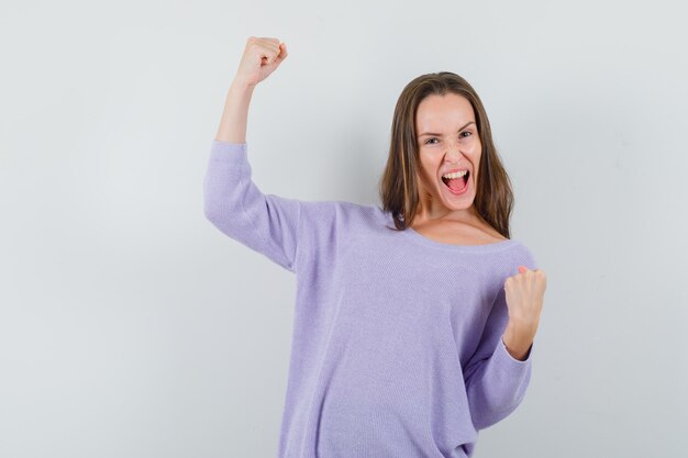 Jonge dame winnaar gebaar in casual shirt tonen en op zoek gelukkig. vooraanzicht.