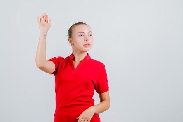 Jonge dame zwaaiende hand terwijl wegkijken in rood t-shirt