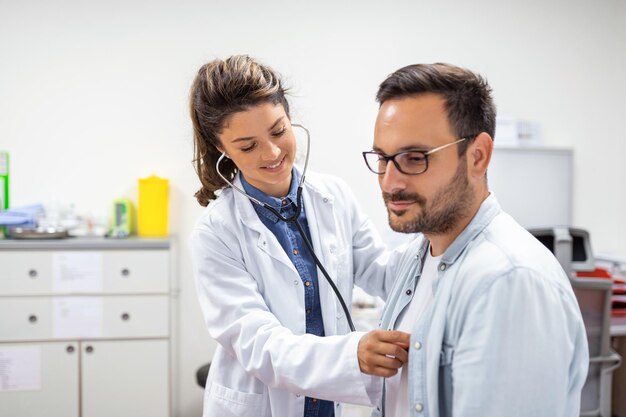 Jonge dokter gebruikt een stethoscoop luister naar de hartslag van de patiënt Shot van een vrouwelijke arts die een mannelijke patiënt een check-up geeft
