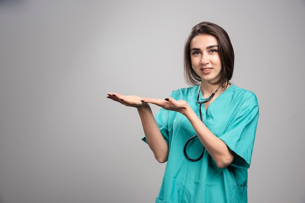 Jonge dokter in uniform gebaren op grijze muur.