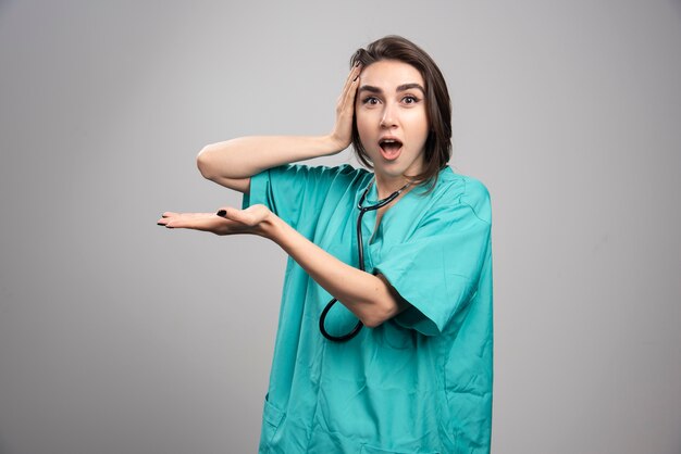 Jonge dokter in uniform verrast op grijze muur.