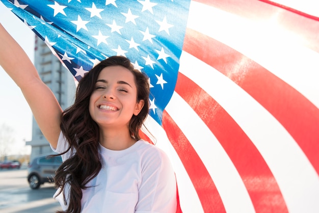 Jonge donkerbruine vrouw die de grote vlag van de VS en het glimlachen houdt