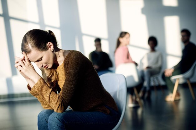 Jonge droevige vrouw die apart zit van de deelnemers aan groepstherapie in het gemeenschapscentrum